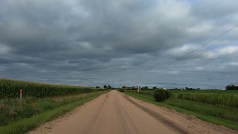 POV-while-driving-on-a-rural-gravel-road-with-pivot-irrigation-equipment,-power-lines,-telephone-lines-and-farm-houses-along-the-road