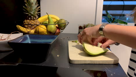Girl-cutting-a-pear-on-a-wooden-board-on-the-black-tabletop