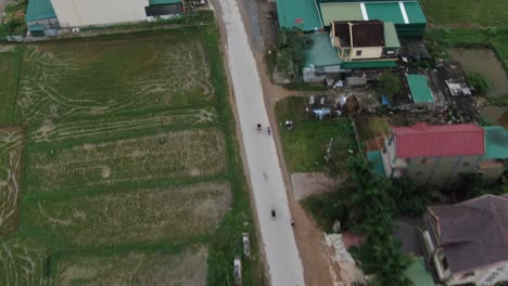 Countryside-drone-birds-eye-view-of-motorbike-driving-in-straight-long-highway-between-houses-and-rice-field-in-rural,-Vietnam
