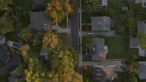 top-down-view-of-suburban-neighborhood-in-fall-at-sunset-slow-crawl-up-as-car-drives-down-the-street