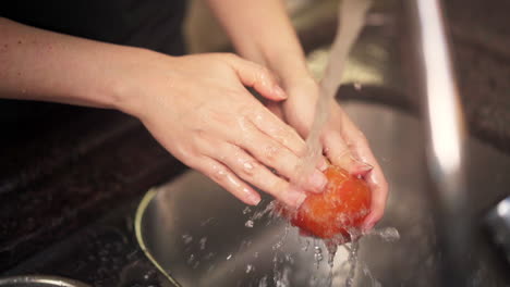 Slow-motion-shot-of-female-hands-washing-a-tomato-under-water-from-a-kitchen-tap