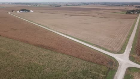 Vista-Aérea-De-La-Conducción-De-Camiones-Desde-La-Intersección-De-Dos-Caminos-De-Grava-En-La-Zona-Rural-De-Iowa