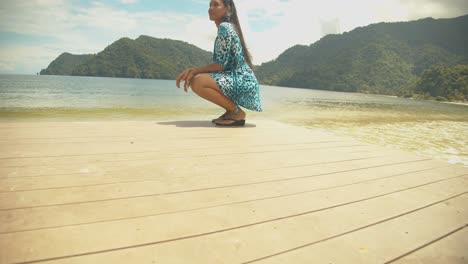 A-model-posing-in-a-sitting-position-on-a-jetty-with-the-beach-and-mountains-in-the-background