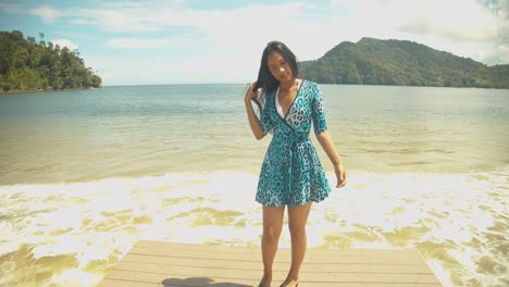 A-girl-in-a-short-dress-on-a-jetty-with-waves-crashing-at-the-shoreline-and-mountains-in-the-background-on-the-Caribbean-island-of-Trinidad