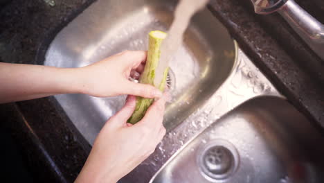 Frauenhände-Waschen-Eine-Grüne-Zucchini-In-Der-Küche-In-Zeitlupe,-Draufsicht