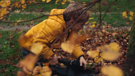 Young-boy-in-yellow-coat-uses-electric-leaf-blower-on-lawn
