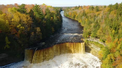 Aerial,-powerful-waterfall-with-viewing-platform-in-fall-forest,-pedestal-up-tilt-down