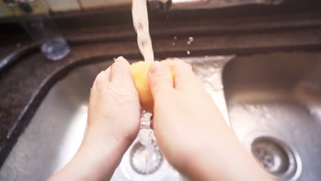Zeitlupenaufnahme-Von-Weiblichen-Händen,-Die-Eine-Kartoffel-Unter-Wasser-Aus-Einem-Küchenhahn-Waschen