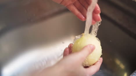 Female-hands-washing-a-white-onion-in-the-kitchen-sink-in-slow-motion