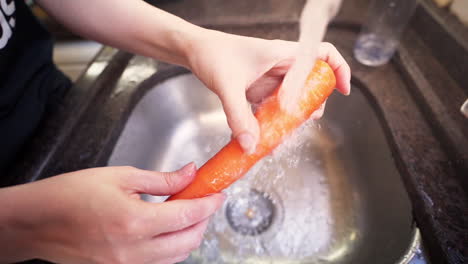 Manos-Femeninas-Lavando-Algunas-Zanahorias-Bajo-El-Agua-De-Un-Grifo-De-Cocina-En-Cámara-Lenta
