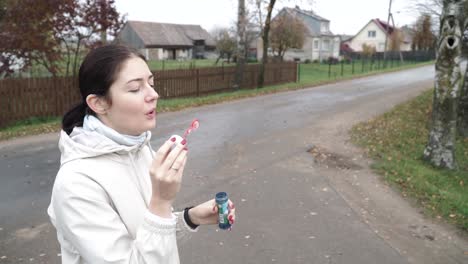 Side-shot-of-young-female-blowing-soap-bubble-outdoor-wind-blows-away-on-the-street-in-the-autumn
