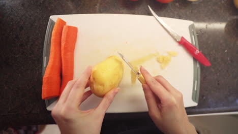 Woman-peeling-potatoes-in-the-kitchen-in-slow-motion,-top-view
