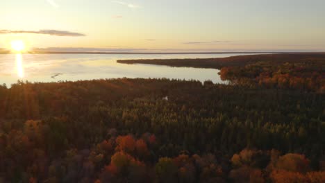 Aerial,-slow-turn-to-reveal-sunset-over-lake-next-to-autumn-forest