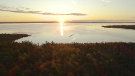 Aerial-pullback,-woods-with-fall-foliage,-sunset-over-large-lake-in-background