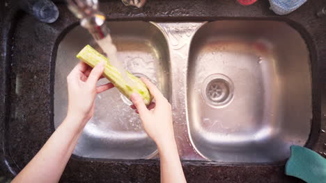 Frauenhände-Waschen-Eine-Grüne-Zucchini-In-Der-Küche-In-Zeitlupe,-Draufsicht