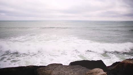 Aerial-view-of-ocean-waves-crashing-against-rocks-on-a-cloudy-day