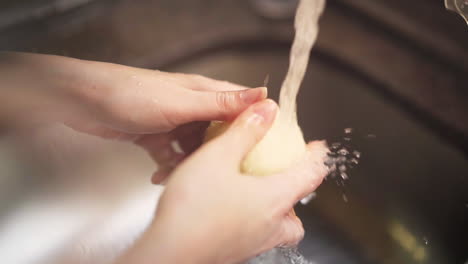 Slow-motion-shot-of-female-hands-washing-a-onion-under-water-from-a-kitchen-tap