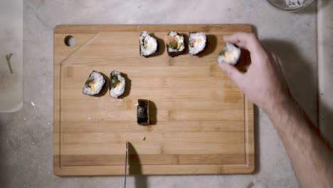 Time-lapse-of-top-down-view-on-two-hands-on-wooden-cutting-tablet-on-kitchen-counter-cutting-a-Sushi-roll-into-pieces