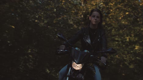 Front-view-of-beautiful-European-Female-motor-Biker-wearing-leather-jacket-On-road-with-autumn-leaf-colored-Trees-at-amelisweerd-forest-on-sunny-day