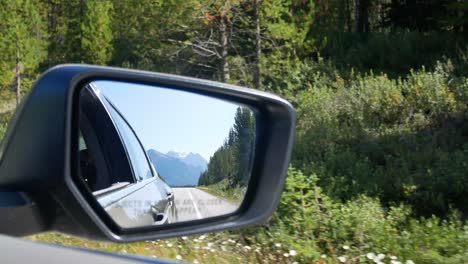 View-of-side-mirror-of-the-moving-car-on-the-local-road-moving-along-the-local-way-through-the-Banff-National-park-in-Alberta,-Canada