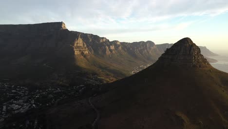 Filmische-Luftaufnahme-Eines-Absteigenden-Krans-Des-Tafelberg-nationalparks-Von-Kapstadt-Und-Des-Löwenkopfgipfels-Während-Des-Sonnenuntergangs-Zur-Goldenen-Stunde