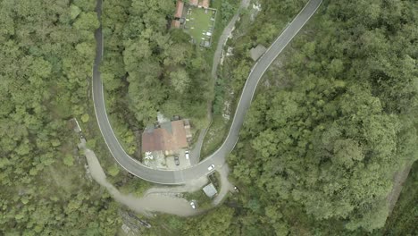 Top-down-aerial-shot-over-Isola-Santa,-white-car-driving-around-curved-road-in-middle-of-dense-forest-in-Italian-mountain-village-in-Tuscany