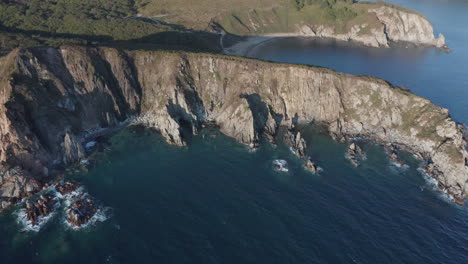 Bird's-eye-view-of-coastline-with-steep-cliffs-and-sandy-beach-bay-on-the-sunset