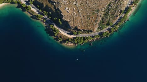 Aerial-dolly-shot-drone-footage-of-cars-driving-on-a-coastal-road-on-a-peninsula-along-a-beautiful-bay-with-crystal-clear-water