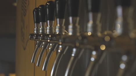 Shiny-chrome-beer-taps-ready-to-fill-up-some-pints,-depth-of-field,-slow-motion
