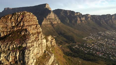 Cinematic-Aerial-Fly-By-Shot-of-Cape-Town's-Lions-Head-Peak-Revealing-Table-Mountain-National-Park-and-Camps-Bay-During-Golden-Hour-Sunset