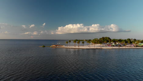 Aerial,-man-made-sandy-point-waterfront-with-palm-trees-and-calm-ocean