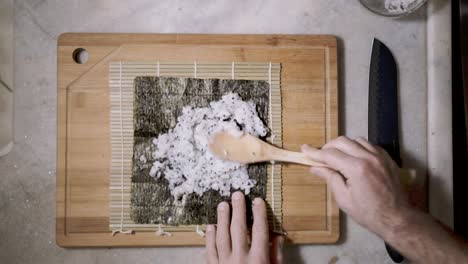 Top-down-time-lapse-of-two-hands-spreading-rice-with-chai-seeds-on-a-mat-and-seaweed-Nori-sheet-to-make-Sushi