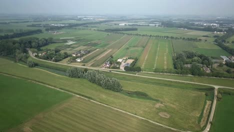 Aerial-drone-shot-of-the-road-alongside-the-farm-fields-in-4K