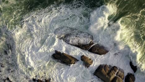 Mezmerizing-Cinematic-Cenital-Gentle-Rise-Shot-of-Rough-Ocean-Waves-Hitting-Rocks-During-Sunset-at-Cape-Town's-Camps-Bay-Beach