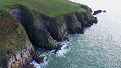 Aerial-view-of-colourful-rugged-sea-cliffs-with-farmland-eroded-on-a-calm-day-in-the-South-of-Ireland