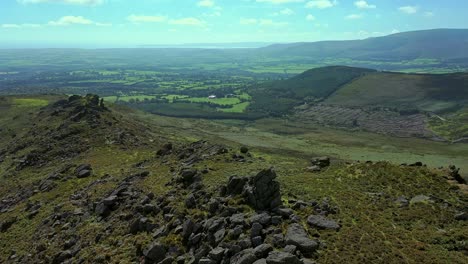 Aerial-orbit-view-of-rock-outcrop,-ridge-line-and-valley-with-view-into-the-distance-over-the-South-of-Ireland-farmland-and-Valley