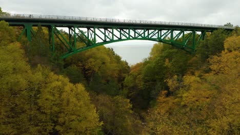 Drone-flies-towards-green-bridge-with-colorful-leaves-on-trees