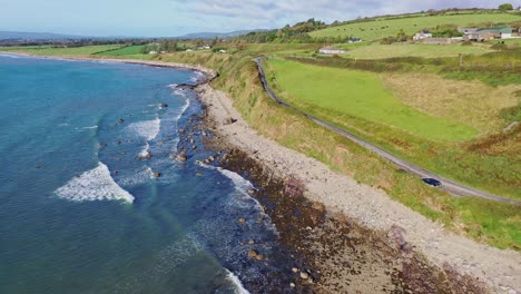 descending-aerial-view-of-waves,-rocky-shoreline-and-costal-road-along-the-South-coast-of-Ireland