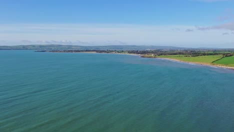 aerial-panoramic-of-the-South-of-Ireland-coastline-made-up-of-farmland-and-cliffs-with-the-sun-reflecting-off-the-calm-Atlantic-ocean-in-Summer