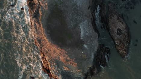Vogelperspektive-Luftaufnahme-Von-Wellen,-Die-Bei-Sonnenuntergang-Gegen-Einen-Felsvorsprung-Schlagen