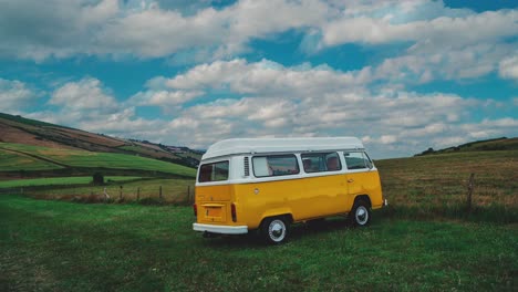 4K-UHD-Cinemagraph---seamless-video-loop-of-a-classic-Volkswagen-VW-T2-Bulli-Camper-Van-standing-on-a-green-field-on-a-sunny-afternoon-in-England-with-blue-sky,-the-clouds-are-moving-by-quickly