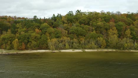Aerial-tracking-shot-of-trees-along-coast-with-reveal-of-green-bridge-during-peak-fall-foliage