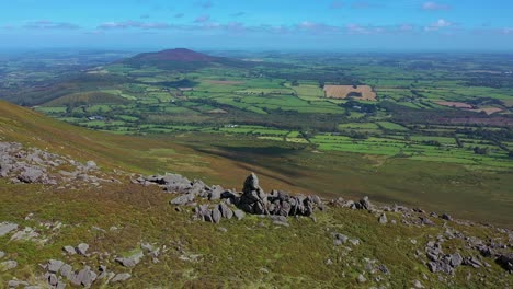 Aerial-orbit-view-of-rock-outcrop,-ridge-line-and-valley-with-view-into-the-distance-over-the-South-of-Ireland-farmland