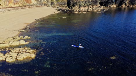 Aerial-view-of-Stand-up-paddle-boarding-in-clear-water-from-a-beach-along-the-rocky-South-Coast-of-Ireland