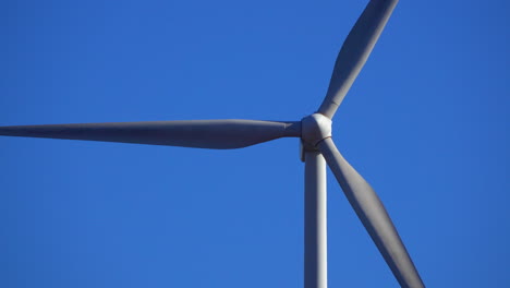 Close-up-telephoto-view-of-a-wind-turbine-spinning-against-a-deep-blue-sky