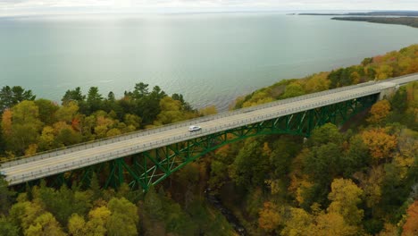 Aerial-circling-shot-of-green-bridge-along-coast-during-peak-fall-foliage