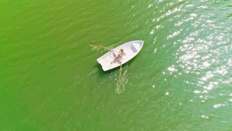 Aerial-view-of-a-young,-beautiful-and-sexy-woman-wearing-bikini,-rowing-alone-a-white-boat-in-the-sea