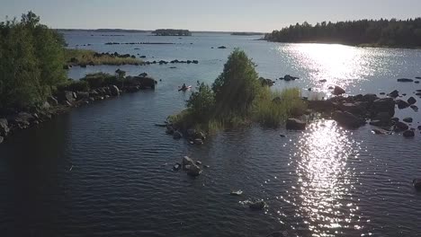 Slow-motion-drone-shot-of-man-kayaking-in-sun-reflected-waters-in-rocky-archipelago,-Ostrobothnia,-Finland