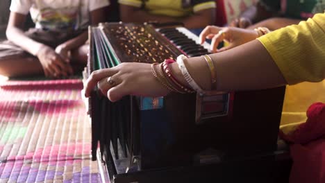 Married-Indian-teacher-playing-music-with-harmonium-at-classroom,-students-learning-music,-unrecognizable