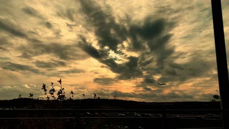 Plane-approaches-for-landing-at-sunset,-flies-low-above-the-highway,-lots-of-clouds-in-the-sky